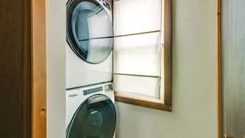A laundry room with two Whirlpool washers, a wooden door frame, and a window.