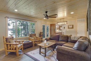 A cozy living room with wooden furniture, large windows, and a ceiling fan.