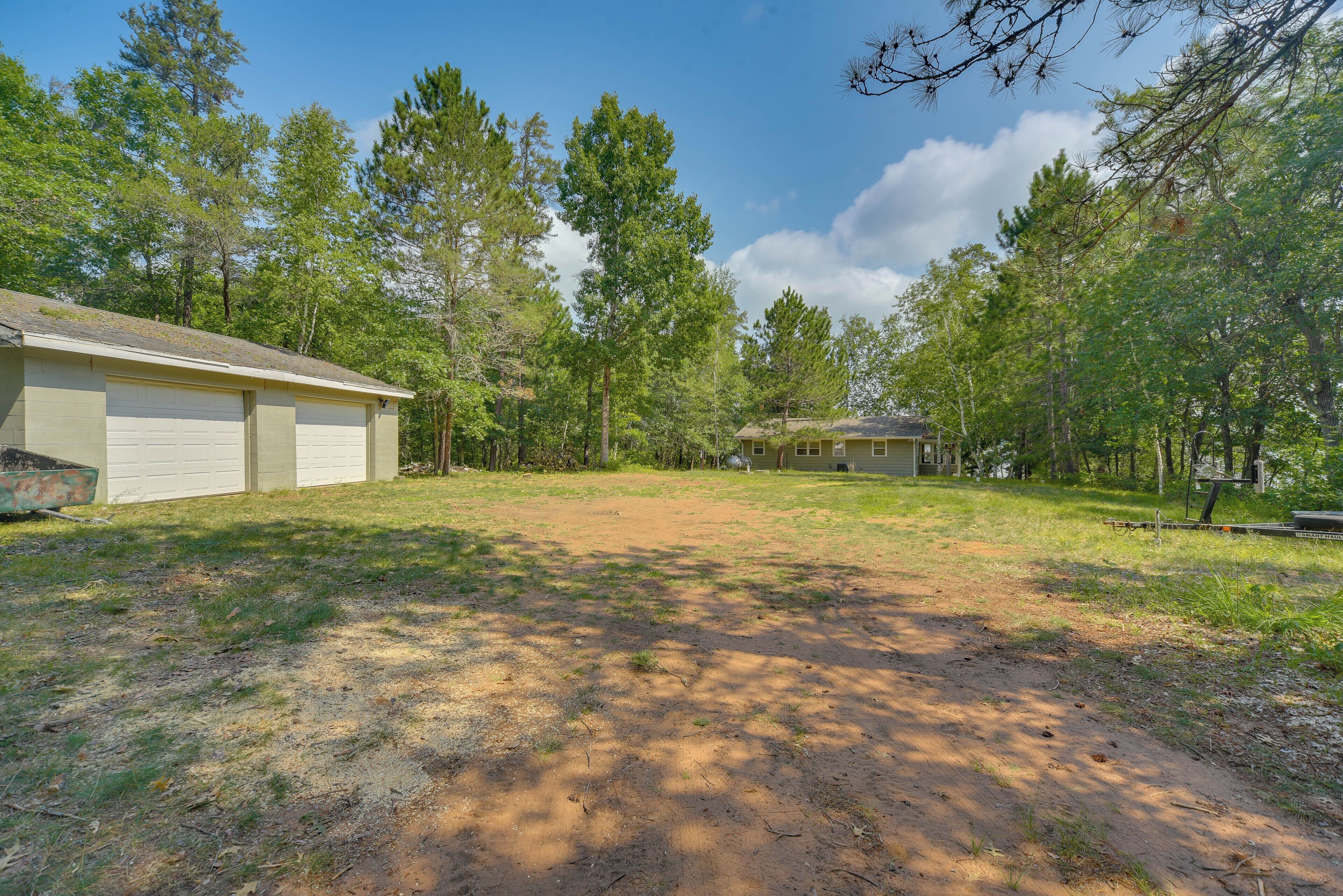 A residential property with a garage, a detached house, and a yard surrounded by trees.