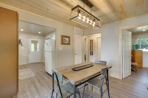 A spacious kitchen with a wooden table and bar stools, a hanging light fixture, and a view into the dining area.