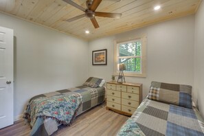 A bedroom with two single beds, a dresser, a ceiling fan, a window with a view, and a door.