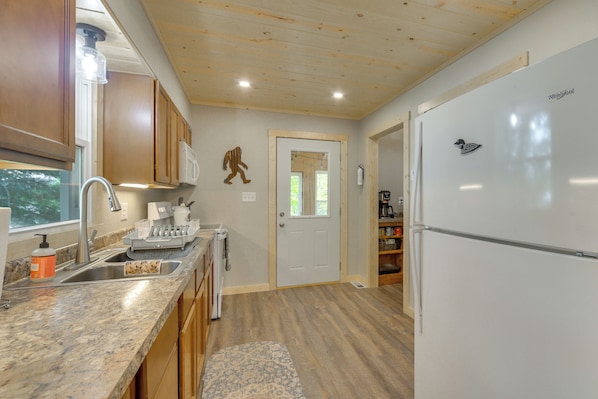 A kitchen with wooden cabinets, a stainless steel sink, a white refrigerator, and a patterned rug.