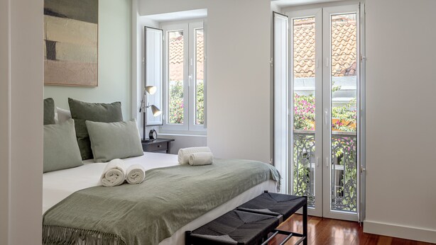 Ein Schlafzimmer mit einem Bett, Kissen, einem Nachttisch mit Lampe und einem Fenster mit Blick nach draußen.
