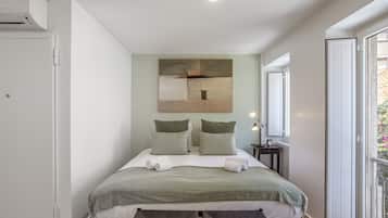 A bedroom with a bed, pillows, a bedside table with a lamp, and a window.