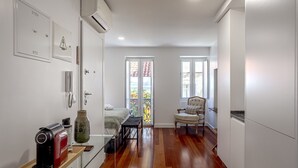 Una habitación compacta con una cama, una silla, una mesita con hervidor y una ventana con vistas a un balcón.