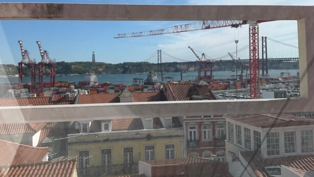 Vista a través de una ventana que muestra un edificio con tejado de tejas, una grúa y un puente al fondo.