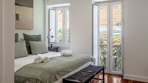 Un dormitorio con cama, almohadas, una mesita de noche con lámpara y una ventana con vistas al exterior.