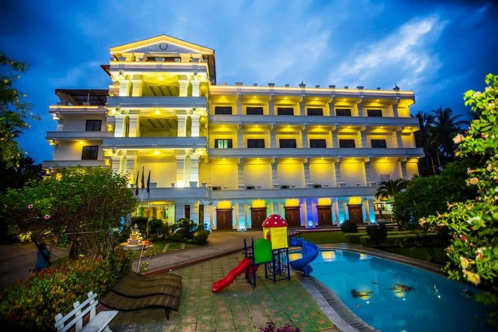 Un hotel de varios pisos con piscina, zona de juegos para niños y un jardín bien cuidado.