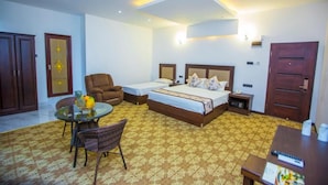 Habitación de hotel con una cama, un escritorio, una silla, una mesita con frutero y una alfombra estampada.