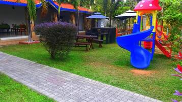 Zona de juegos infantiles con tobogán, mesas de picnic y un área de descanso cubierta.