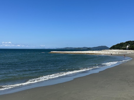 A beach with a stone breakwater, clear skies, and distant mountains.