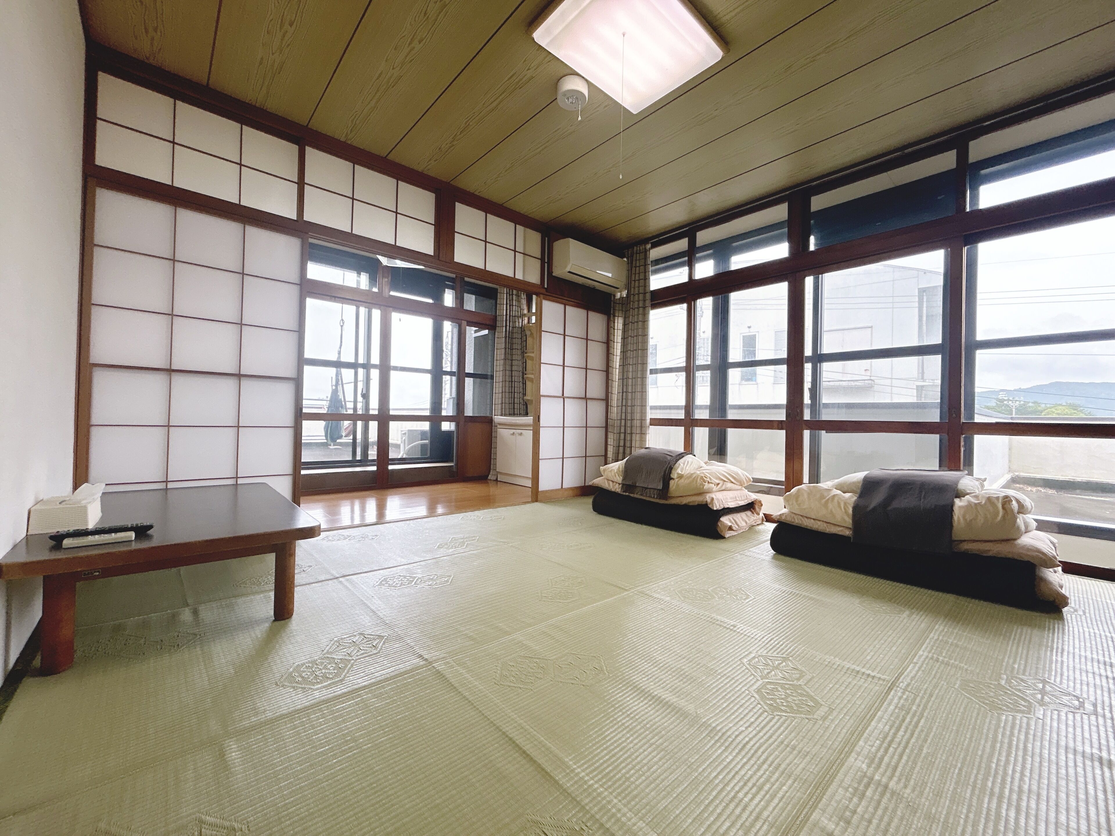Habitación con tatami, una mesa baja, camas futón y ventanas amplias.