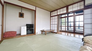A traditional Japanese room with tatami flooring, a television, a small table, and a sliding door with a view.