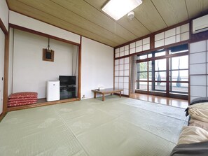 A traditional Japanese room with tatami flooring, a television, a small table, and a sliding door with a view.