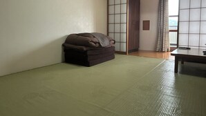 A traditional Japanese room with tatami flooring, a low brown sofa, a sliding shoji screen, and a wooden table.