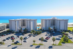 A hotel with a central courtyard, multiple parking spaces, and a view of the ocean. - Family Friendly Gulf Front Condo at Regency Towers with Pool & Tennis (Pensacola Beach)
