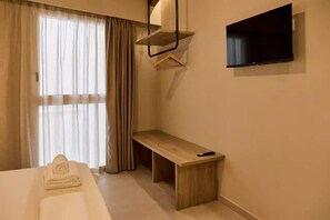 Habitación de hotel con cama, mesita de noche, control remoto, televisor montado en la pared y ventana con cortinas.