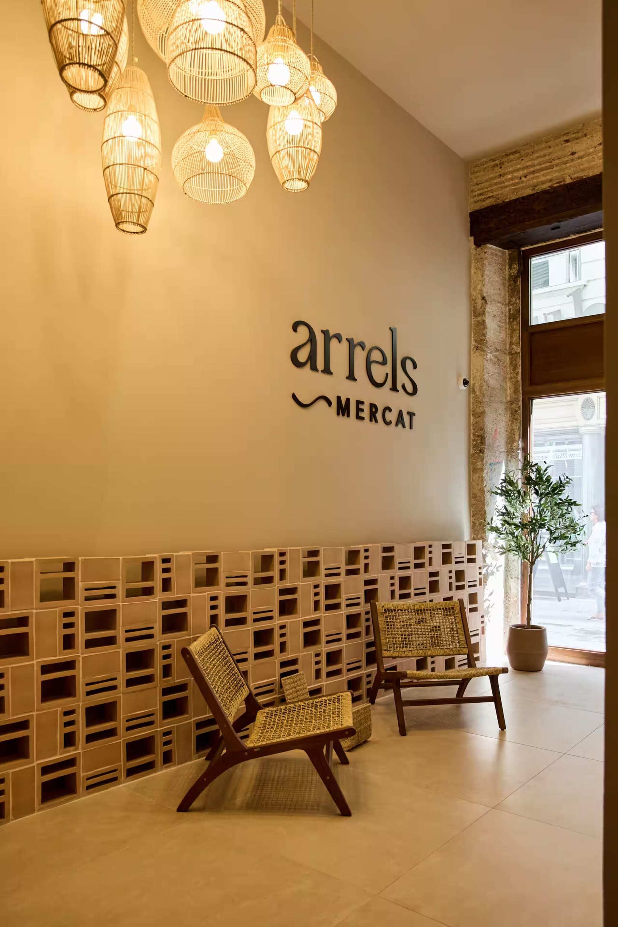 Ein Empfangsbereich mit Korbstühlen, einem an der Wand befestigten Schild mit der Aufschrift 'arrels mercat' und hängenden Korbstühlenlampen.
