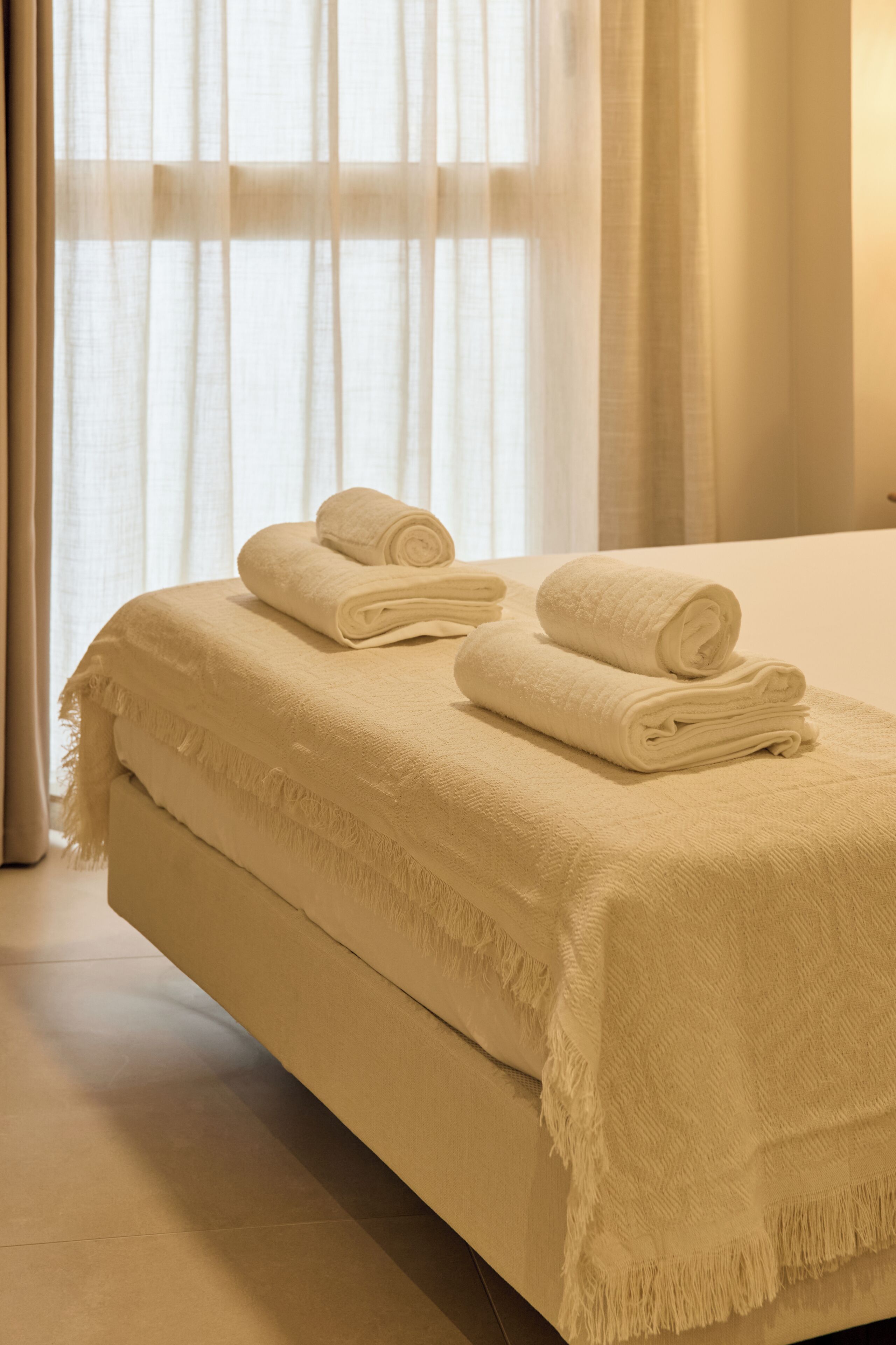 Una cama con una manta color beige y dos toallas enrolladas.