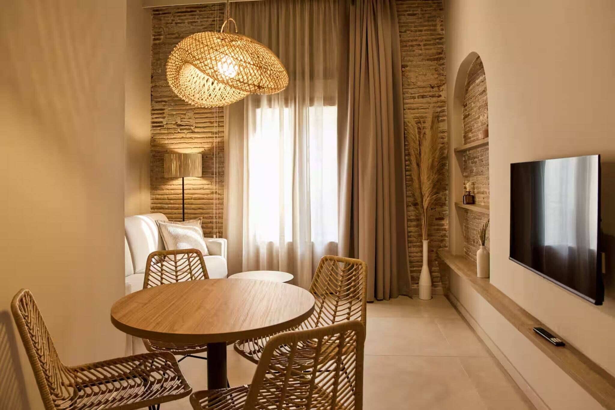 Una sala de estar moderna con una mesa redonda de madera, sillas de mimbre, una lámpara colgante grande de tejido, un televisor de pantalla plana en la pared y una pared con textura de piedra.