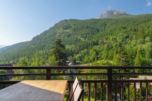 A wooden deck with a table and chairs, overlooking a mountainous landscape with dense forest and a clear sky. - Le Soleil Bleu • Spacious ski-in/ski-out apartment in Serre Chevalier (Saint-Chaffrey)