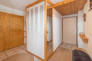 A room with a sliding wooden door, a white closet with louvered doors, a wooden ceiling, and a small shelf with toiletries. - Le Soleil Bleu • Spacious ski-in/ski-out apartment in Serre Chevalier (Saint-Chaffrey)