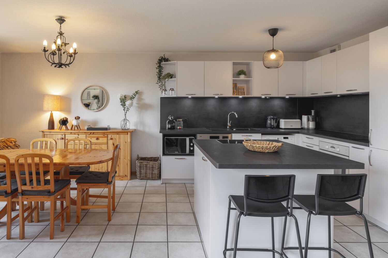 A modern kitchen with a central island, white cabinetry, and a dining area with wooden furniture.