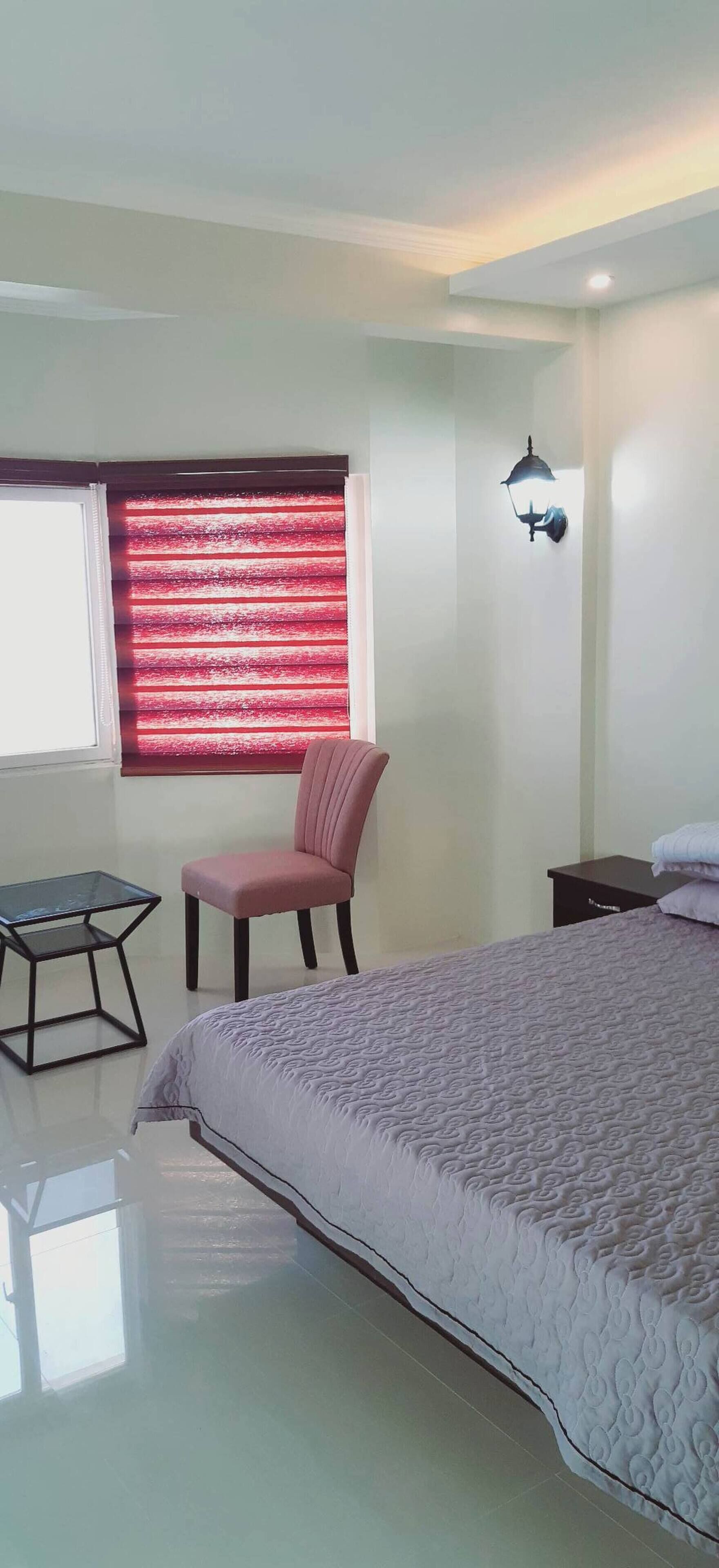 Een slaapkamer met een bed, een stoel, een klein tafeltje en een raam met rode luiken.