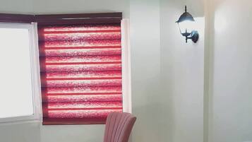 Een slaapkamer met een bed, een stoel, een klein tafeltje en een raam met rode luiken.