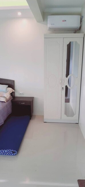 Un dormitorio con cama, armario, mesita y aire acondicionado.
