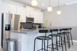 A modern kitchen with white cabinets, stainless steel appliances, and a central island with bar stools. - Luxury 4BR at ChampionsGate w/ Private Pool & BBQ (Davenport)