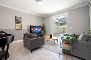 Una sala de estar moderna con un sofá gris, un televisor de pantalla plana y una mesa de comedor.