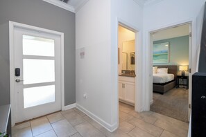 A hallway leading to a bedroom with a bed, a nightstand, and a lamp. There is a bathroom with a shower and a sink visible through an open door. - Luxury 4BR at ChampionsGate w/ Private Pool & BBQ (Davenport)