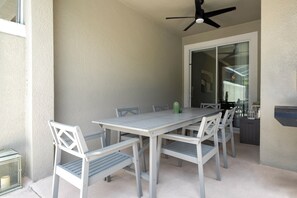 A covered patio with a table and chairs, a ceiling fan, and a sliding glass door leading to an interior space. - Luxury 4BR at ChampionsGate w/ Private Pool & BBQ (Davenport)