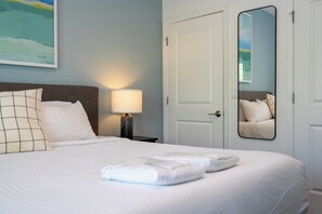 Una habitación de hotel con una cama, una mesita de noche, una lámpara, un espejo y una puerta.