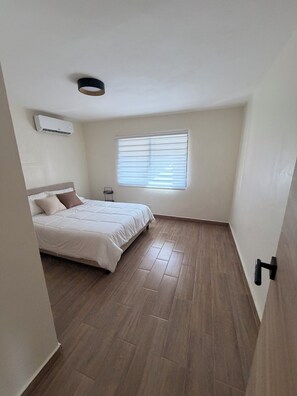 Ein Schlafzimmer mit einem Bett, einem Fenster mit Jalousien, einer Klimaanlage und einem Holzboden.
