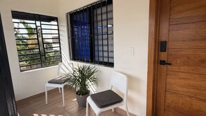 A room with a wooden door, two white chairs, a potted plant, and a window with metal bars. - Modern apartment stay in Santo Domingo (Santo Domingo)