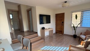 A modern living room with a dining area, a TV mounted on the wall, and a staircase leading to another level. - Modern apartment stay in Santo Domingo (Santo Domingo)