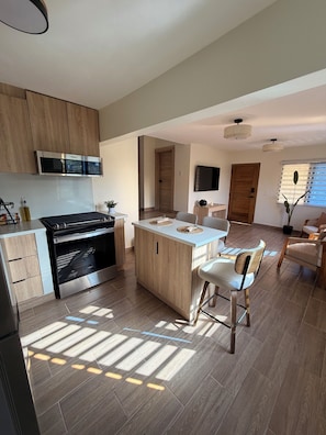 Eine moderne Küche mit Einbauofen, einem Essbereich mit zentraler Kochinsel und einer Sitzecke inklusive Sofa und Stühlen.