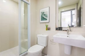 A modern bathroom with a glass shower enclosure, a white toilet, a sink with a mirror, and a framed picture on the wall. - Pattaya Central Excellent 1 Bed Room Excellent Location (Pattaya)