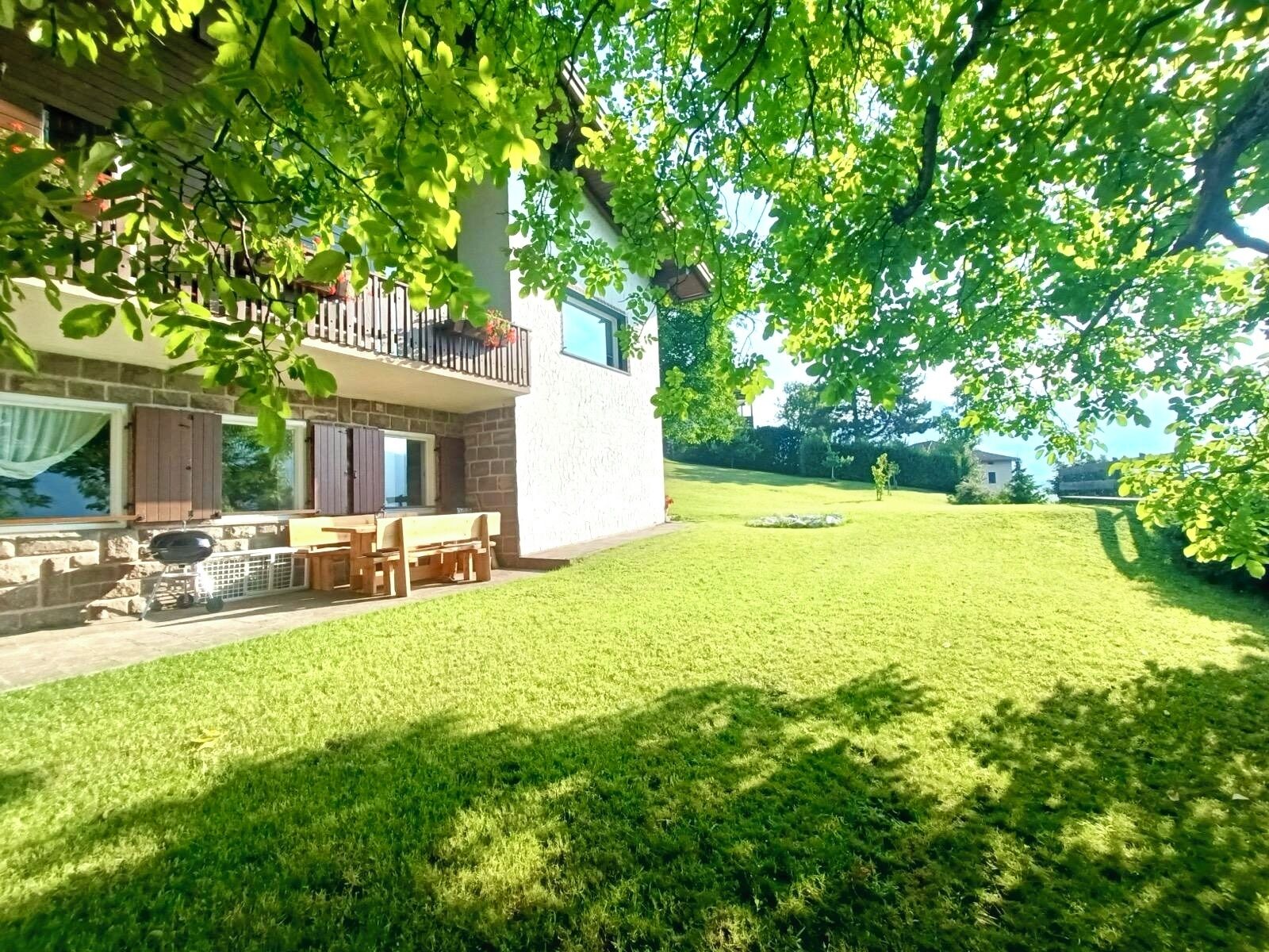 Ein zweigeschossiges Haus mit Balkon, Grill und gepflegtem Rasen.