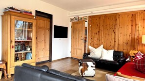 Un salon avec un canapé en cuir noir, un meuble en bois doté de portes en verre, une armoire en bois et un téléviseur fixé au mur.