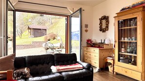 A living room with a leather sofa, a wooden cabinet with glass doors, and a view of a garden through a sliding glass door. - Villa ai Noci (Carano)