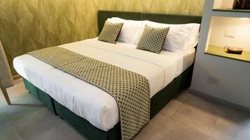 A bed with a patterned bedspread and pillows, a green upholstered headboard, and a bedside table with a lamp.