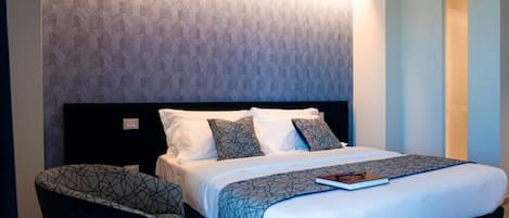 A hotel room with a bed, a chair, and a patterned wall.