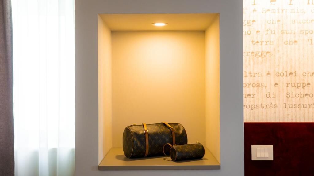 A display case with a bag and a smaller pouch, possibly a Louis Vuitton, against a wall with a light source above.