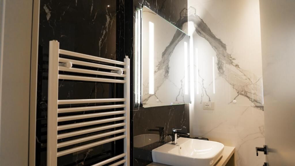 A bathroom with a white bathtub, a white sink, and a mirror reflecting the room's marble wall.