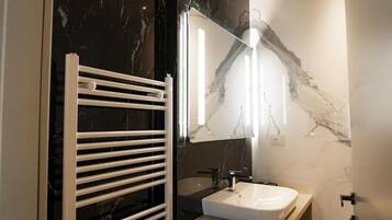 A bathroom with a white bathtub, a white sink, and a mirror reflecting the room's marble wall.