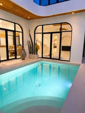 A modern indoor swimming pool with a clear blue water surface, surrounded by a white interior with wooden ceiling accents and large windows. - 2BR Private Pool Villa Walk to Pererenan Beach and Cafes (Mengwi)