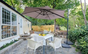 An outdoor patio with a table and chairs, a large umbrella, and a house in the background. - Mountain & Pool Retreat - Pitres Campground (Pitres)